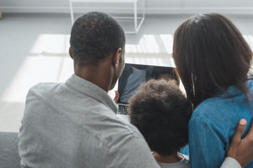 back view of african american parents and son using laptop in living room