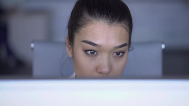 Face of young attractive woman is working in front of monitor in large company, 4k sitting at table, looking at pc screen, touching facial skin. Female secretary in white clothes does work. Concept