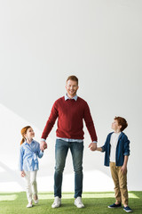Fototapeta premium happy father with adorable smiling kids holding hands while standing on grass