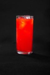 Single-colored, red cocktail in a glass with ice from grapefruit, tomato, strawberry. Side view. Isolated black background. Drink for the menu restaurant, bar, cafe