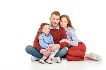 happy parents with cute little daughter sitting together and smiling at camera isolated on white