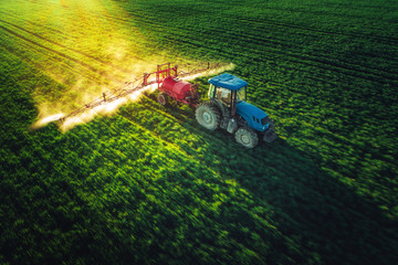Aerial view of farming tractor plowing and spraying on field - obrazy, fototapety, plakaty