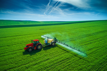 Fototapeta premium Aerial view of farming tractor plowing and spraying on field