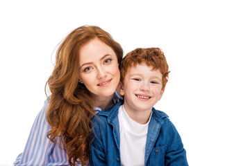 happy red haired mother and son smiling at camera isolated on white