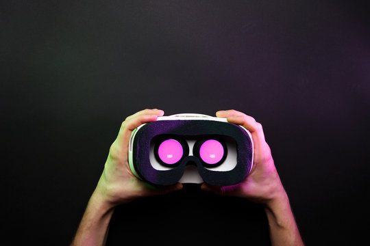 Photo of hands holding virtual reality glasses with burning pink light on black background