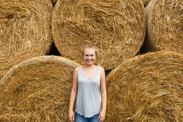 A smiling young woman with blond hair stands on the background of haymaking.