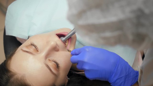 Female dentist treating teeth to young woman patient in clinic.