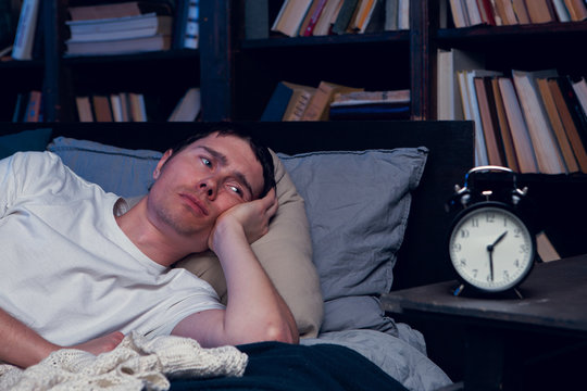 Photo of man with insomnia lying in bed next to alarm clock