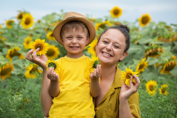 Mom and son hug, laugh and play in a field of sunflowers. Happy family moments spent in the open air. Mother's Day.