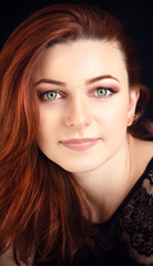 Portrait of a beautiful young woman with long red hair on a dark background