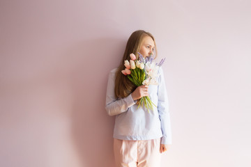 A young beautiful girl with blond dissolved long hair, a felt hat on her head, keeps spring flowers in her hands on a sunny day. Women's Day.