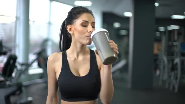 Fit woman drinking protein shake after workout, muscle gain nutrition, health