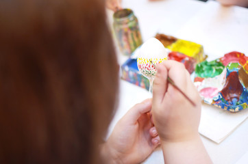  Kinderhände, die weißes Osterei mit bunten Punkten bemalen