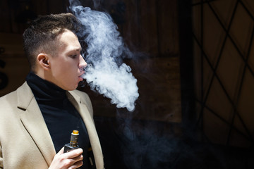 A young guy smokes and exhales a cloud of smoke. Vape