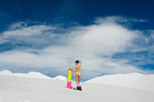 Back view of hot snowboarder woman in a swimsuit with a pink boardon a mountain