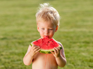 One year old baby boy eating watermelon in the garden