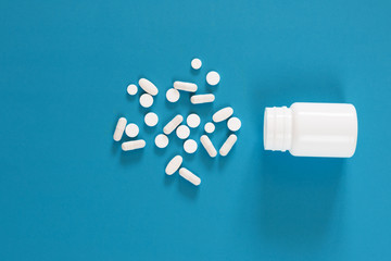 White different tablets spilled from a white plastic bottle on an empty blue background