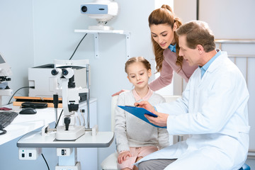 mother and daughter looking at clipboard in ophthalmologist consulting room
