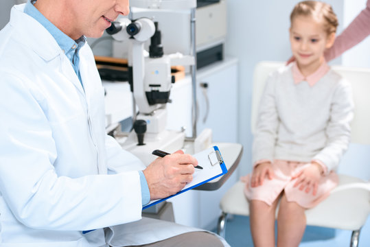 cropped image of ophthalmologist writing something to patient clipboard