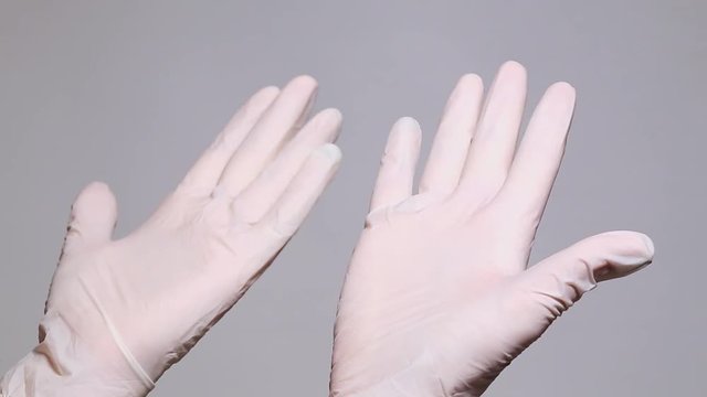 Adult woman looks at her hands in new latex white gloves. Isolated at grey background.