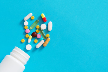 Colorful different tablets spilled from a white plastic bottle on an empty blue back ground