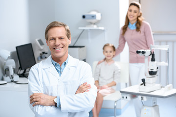 Fototapeta premium smiling ophthalmologist and mother with daughter in consulting room
