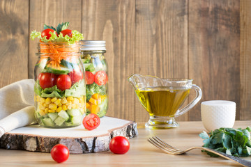 Vegetable healthy homemade colorful salad in mason jar with tomato, lettuce, broccoli on wooden board. Copy space. Lunch for work.