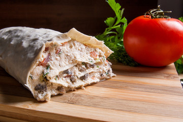 Pita bread or lavash wrapped with cottage cheese or curd, chicken, tomatoes and herbs - dill, onion, parsley on cutting board..