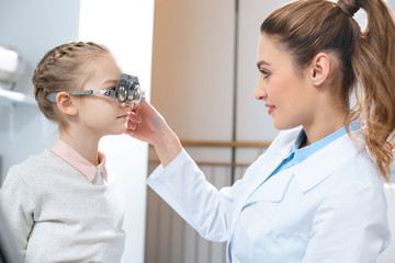 optometrist examining kid eyes with trial frame in clinic