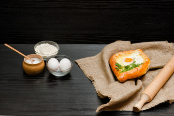 Georgian cuisine. Khachapuri on sackcloth, flour, eggs and rolling pin. Black table. Space for text