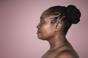 Young African woman standing sideways against an ash rose background