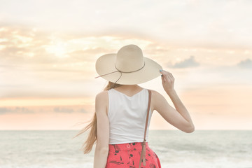 Girl in a hat stand by the sea, sunset. Back view