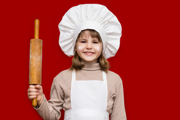 Happy little girl in chef uniform holds rolling pin isolated on red. Kid chef. Cooking Process Concept 
