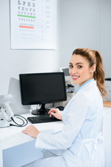 smiling female optician working with computer in clinic