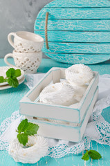Meringues in a white wooden box on a turquoise background