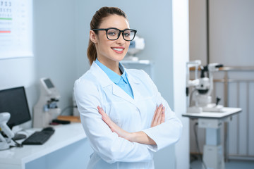 attractive professional ophthalmologist in glasses standing with crossed arms in optical clinic