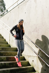 Sporty urban woman running downstairs. Female athlete trainning and exercising in city stairs.