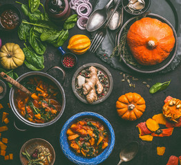 Autumn seasonal food and cooking with pumpkin.  Dark rustic kitchen table  with tools, bowls, spoons, whole and cut pumpkin and meals, top view. Vegetarian food