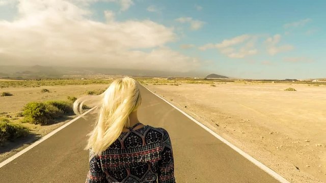 young and caucasian blonde girl  enjoy a sunny day walking on a long infinite road. life and future concept for people that live the world. beautiful place outdoor leisure activity