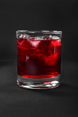 One-color, red transparent cocktail, cold tea in a low glass with ice cubes with the taste of grapefruit, berries, strawberries, cherries. Side view. Isolated black background. Drink for the menu