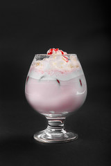 Pina colada, pink creamy cocktail in a low glass with crushed ice frappe with strawberry, cherry, berries, whipped cream and strawberry syrup. Side view. Isolated black background. Drink for the menu