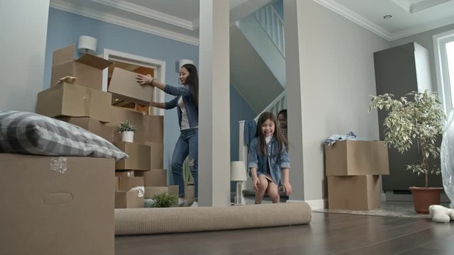 PAN of happy little girls and their mother unrolling carpet and playing while unloading belongings in new house