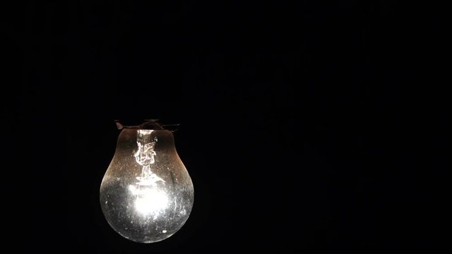 included light bulb slowly swings on the wire. the incandescent lamp is shining in the dark. Slow motion