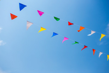 Colorful festive bunting flags against a blue sky and clouds background