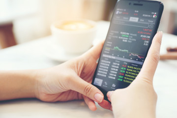 Female hand with smartphone trading stock online in coffee shop , Business concept