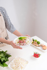 Female chef prepare traditional Vietnamese soup Pho bo with herbs, meat, rice noodles