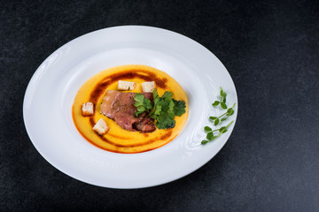 An appetizing pumpkin soup is served in a white plate in a restaurant