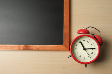 Red vintage alarm clocks close to blackboard on wooden table