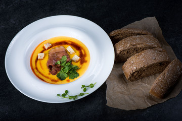 An appetizing pumpkin soup is served in a white plate in a restaurant