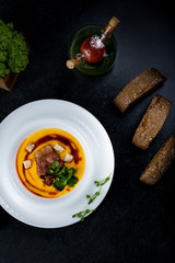 An appetizing pumpkin soup is served in a white plate in a restaurant